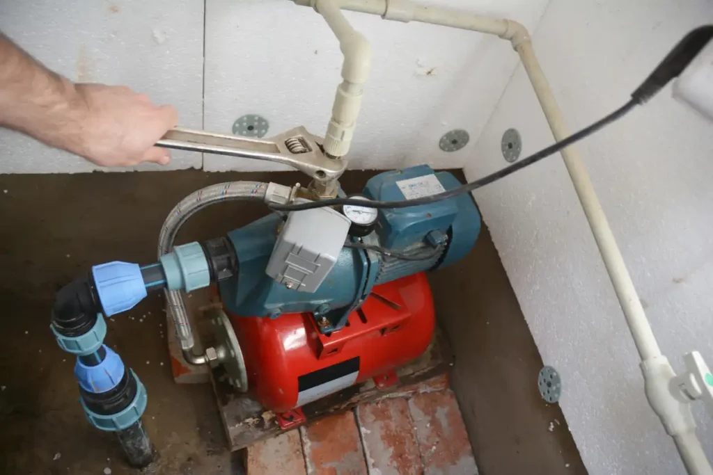 Well Pump Services In Downingtown, PA 1 A person's hand uses a wrench to work on a red and blue water pump connected to white pipes.