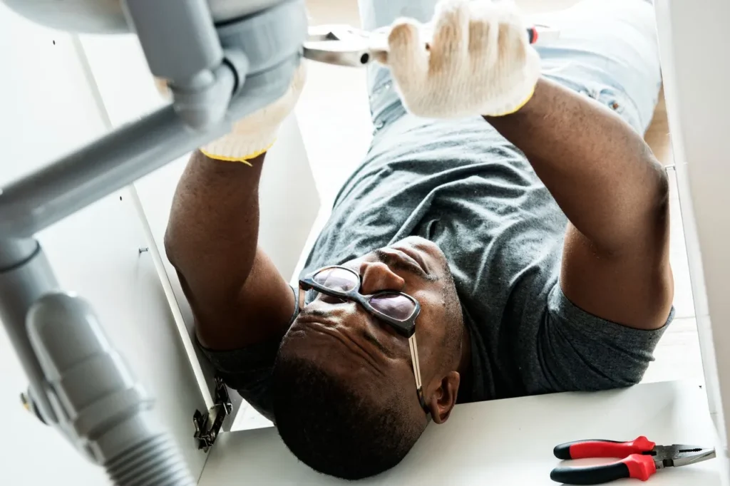 Plumber in Coatesville, PA 1 Man in glasses fixes kitchen sink plumbing.